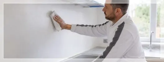 Peintre préparant un mur de cuisine avant peinture
