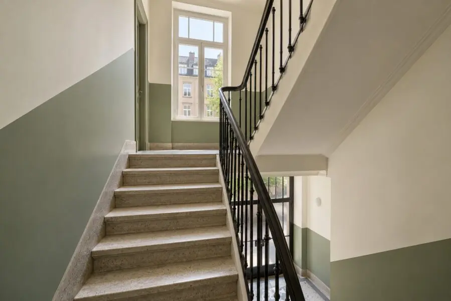 Illustration d’une cage d’escalier rénovée, murs clairs et soubassement vert sauge